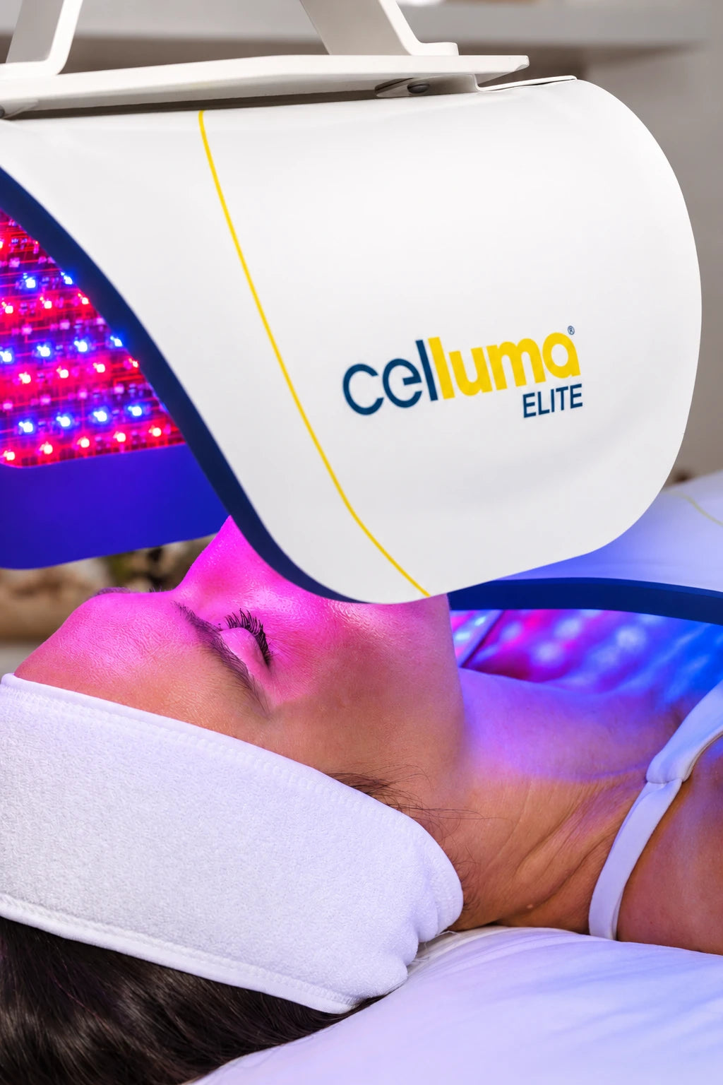 A client receiving a facial treatment beneath an illuminated original Celluma ELITE panel